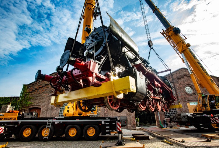 Eine Dampflokomotive wird von zwei Kränen angehoben.