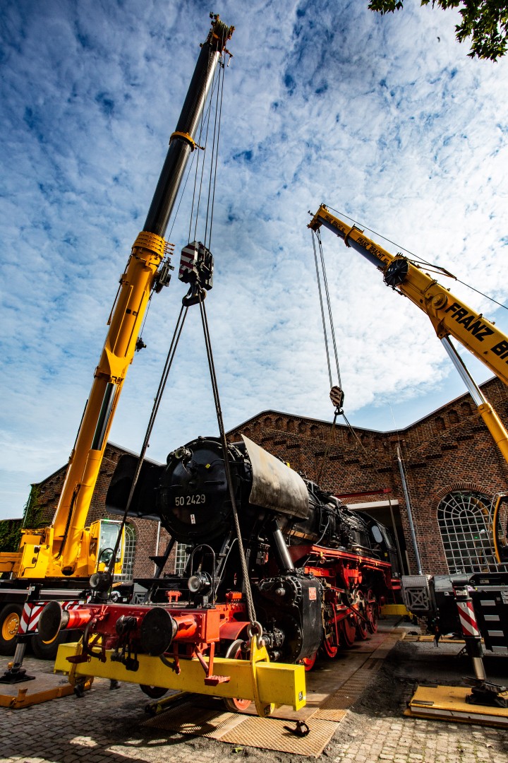 Eine Dampflokomotive wird von zwei Kränen angehoben.