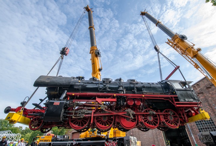 Eine Dampflokomotive wird von zwei Kränen angehoben.