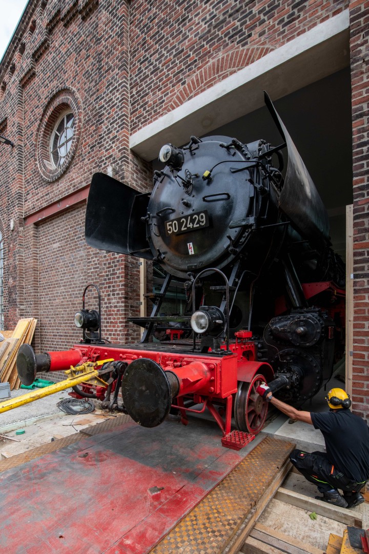 Eine Dampflokomotive ragt aus einem Backsteingebäude.