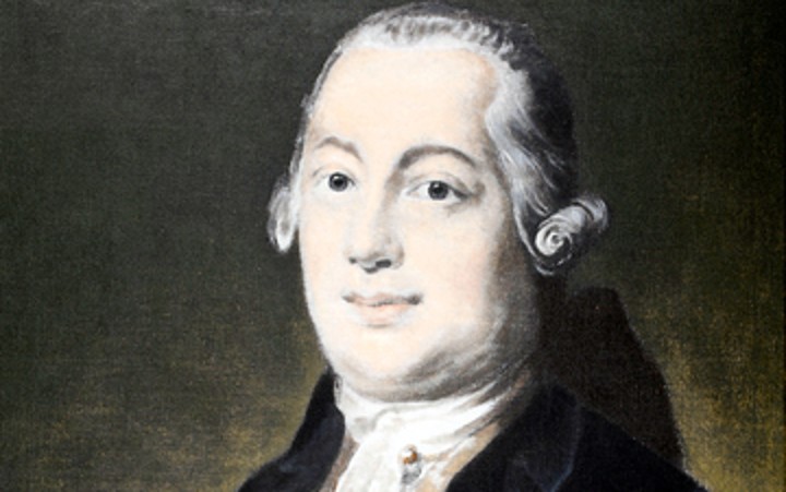 Porträt eines Mannes in historischer Kleidung mit weißem Rüschenhemd und dunklem Jackett vor einem dunklem Hintergrund.