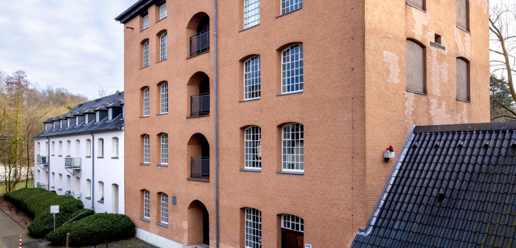 Ein ockerfarbenes Geäude mit vielen Fenstern. Es handelt sich um die Hohe Fabrik der Textilfabrik Cromford.