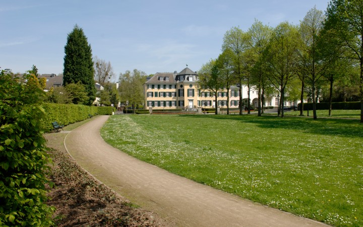Park with path and meadow, at the end an old manor house