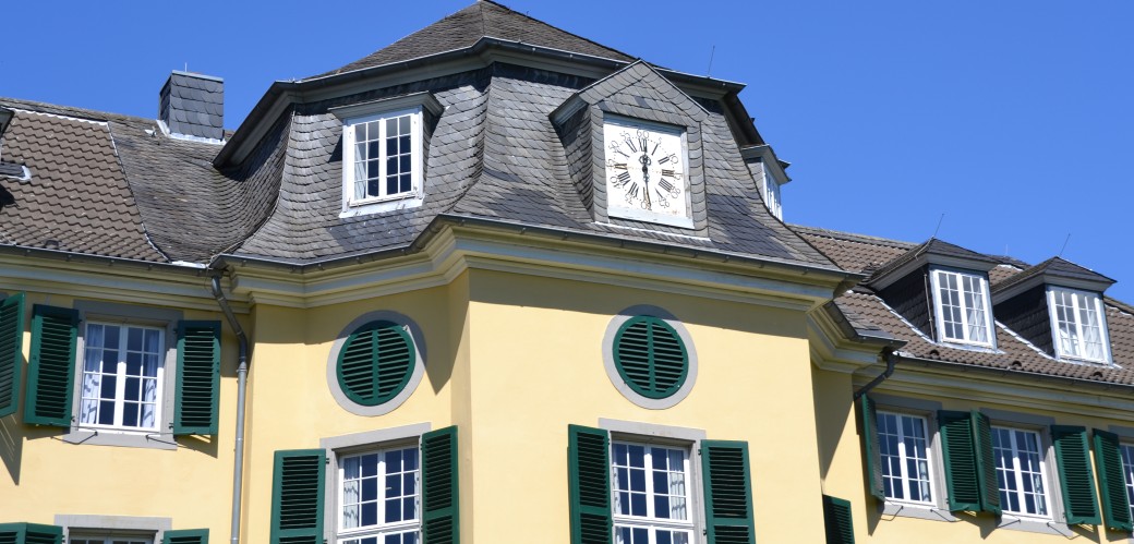 Blick auf Den Giebel des Herrenhauses Cromford mit einer großen, quadratischen Uhr, daneben befinden sich viele Fenster mit dunkelgrünen Fensterläden.