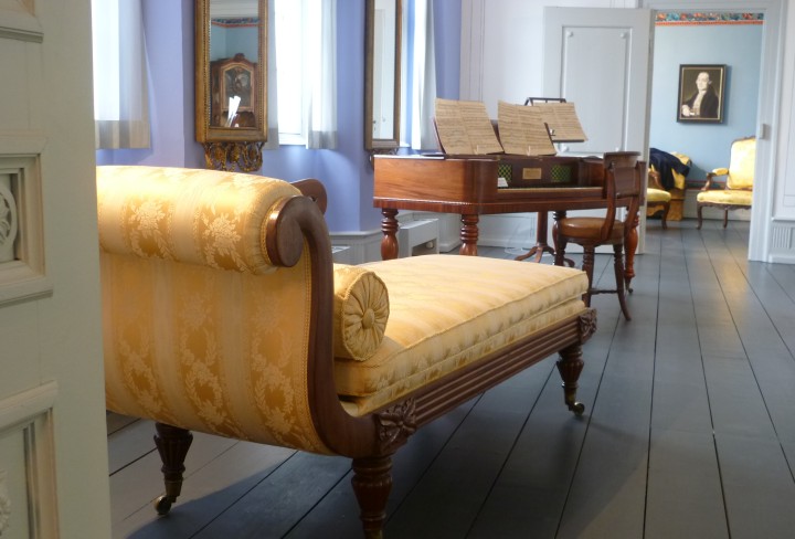 Looking through rooms in the manor house, you can see a yellow sofa and a piano