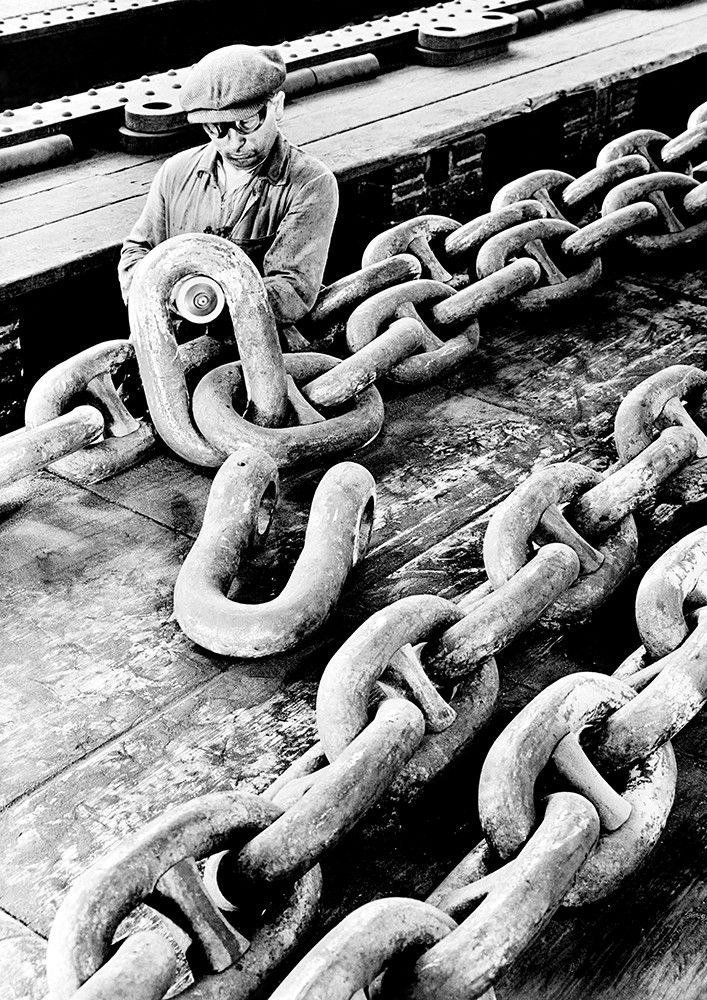 Historisches Schwarzweiß-Foto eines Arbeiters, der eine riesige Kette bearbeitet