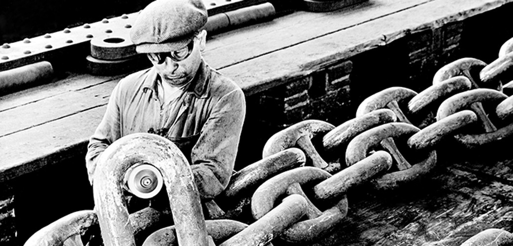 Historisches Schwarzweiß-Foto eines Arbeiters, der eine riesige Kette bearbeitet