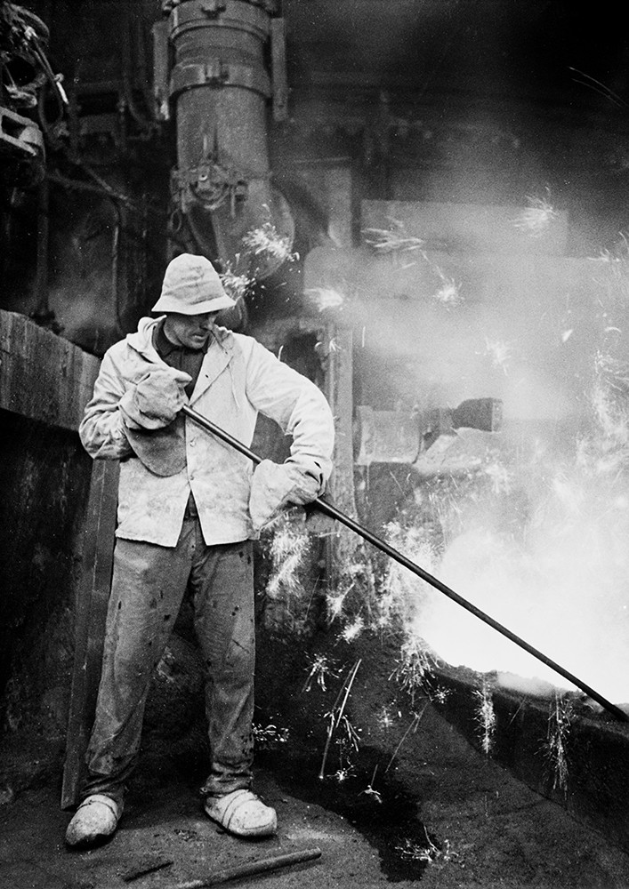 Historisches Schwarzweiß-Foto eines Arbeiters, im Hintergrund Glut und Rauch