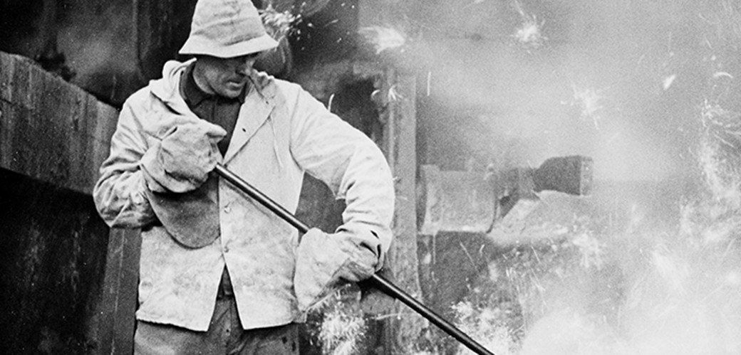 Historisches Schwarzweiß-Foto eines Arbeiters, im Hintergrund Glut und Rauch