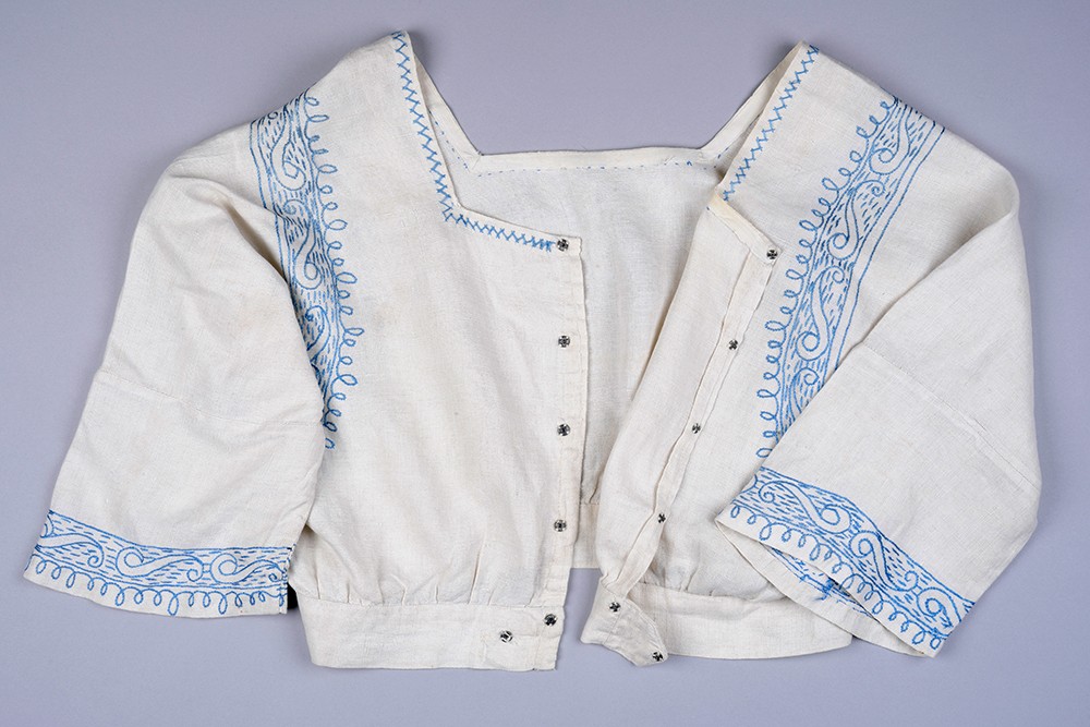 Das Bild zeigt eine Fotografie einer bestickten weißen Bluse aus Baumwolle und Leinen.