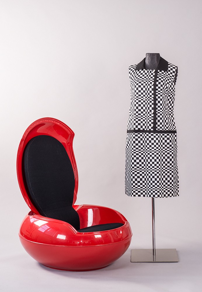 Schwarz-weiß gemustertes, knielanges Kleid an einer Figurine neben einem roten Plastiksessel