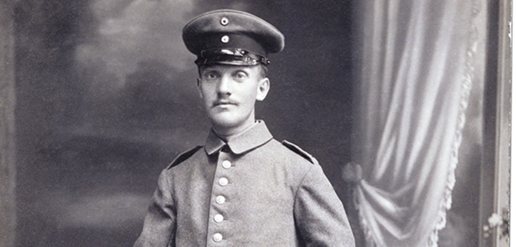 Vorderseite der Fotopostkarte zeigt eine Schwarzweiß-Fotografie eines Soldaten in Uniform