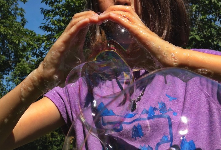 Bild von einem Mädchen, was Seifenblasen in der Hand hat.