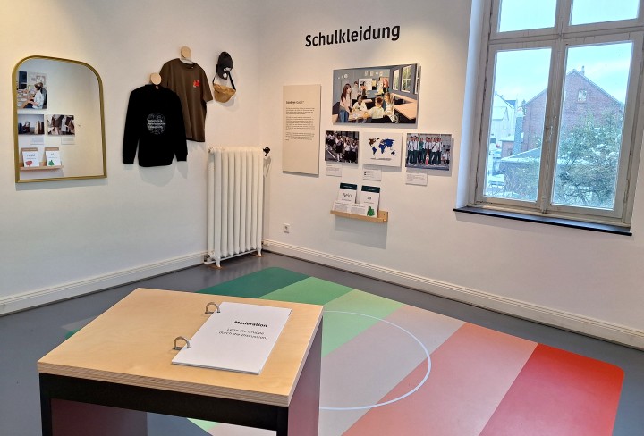 Foto aus einem raum der Ausstellung "Spielräume Demokratie" An der Wand sind Texte und Bilder zum Thema Schulkleidung.