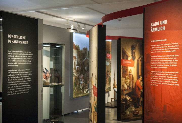  Blick in die Ausstellung mit zwei großen Texttafeln, historischen Bildern und Vitrinen 