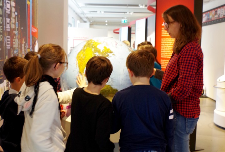 Kinder mit Frau an einem großen Globus in der Ausstellung