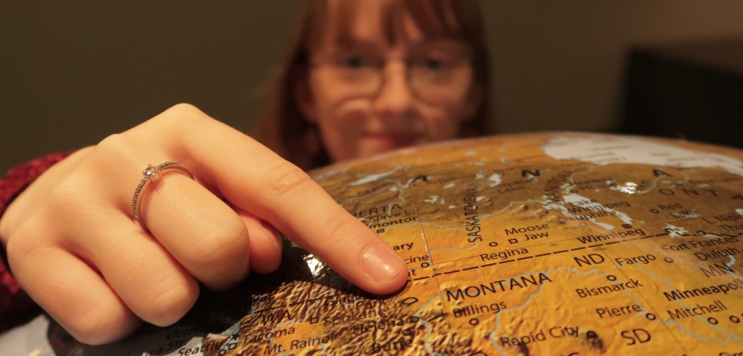 Eine Frau zeigt mit dem Zeigefinger auf einen Globus. 