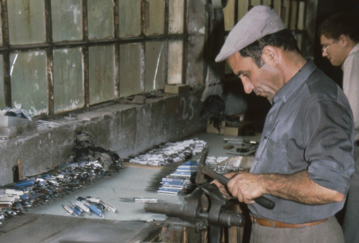 Ein Mann der Taschenmesser fertigt steht vor einem Tisch und hält sein Arbeitswerkzeug in den Händen.