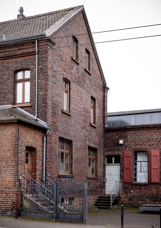 Außenansicht eines roten Backsteinhauses mit mehreren Türen und Fenstern, die in einen Hinterhof führen