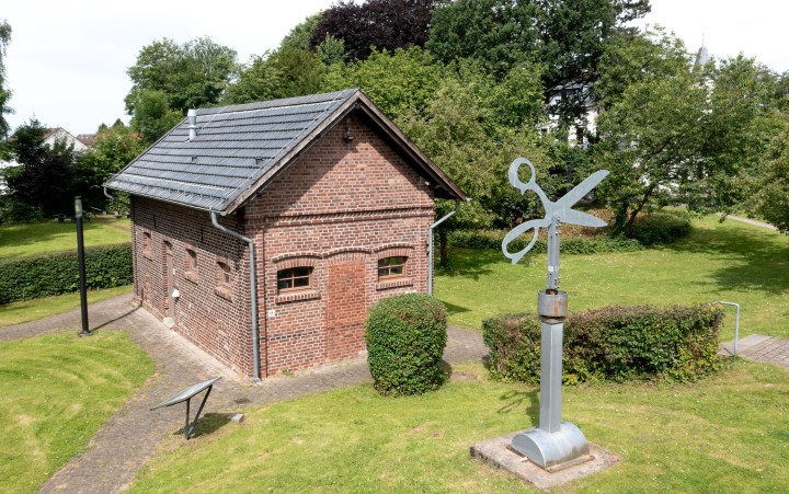 Blick von Oben auf ein Backsteingebäude mit einer Skulptur einer Schere auf einer Säule davor