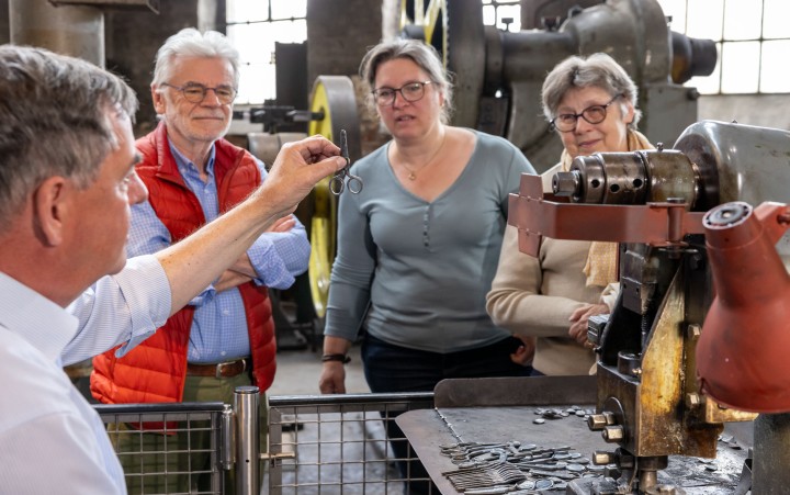 Museumsgästeführer zeigt Besuchenden eine Schere