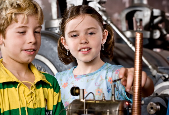 Ein Mädchen und ein Junge blicken interessiert auf ein Modell einer Dampfmaschine 