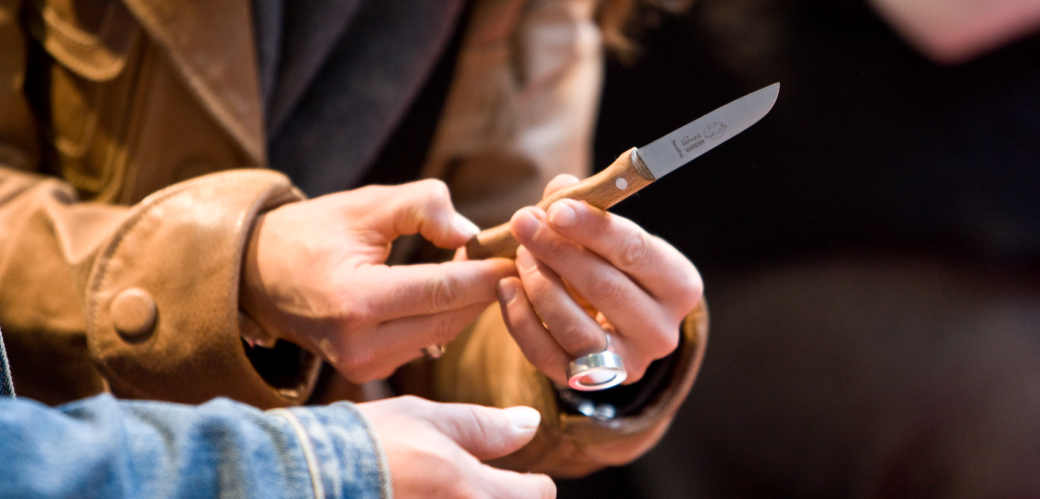 Zwei Hände halten ein kleines Küchenmesser mit Holzgriff.