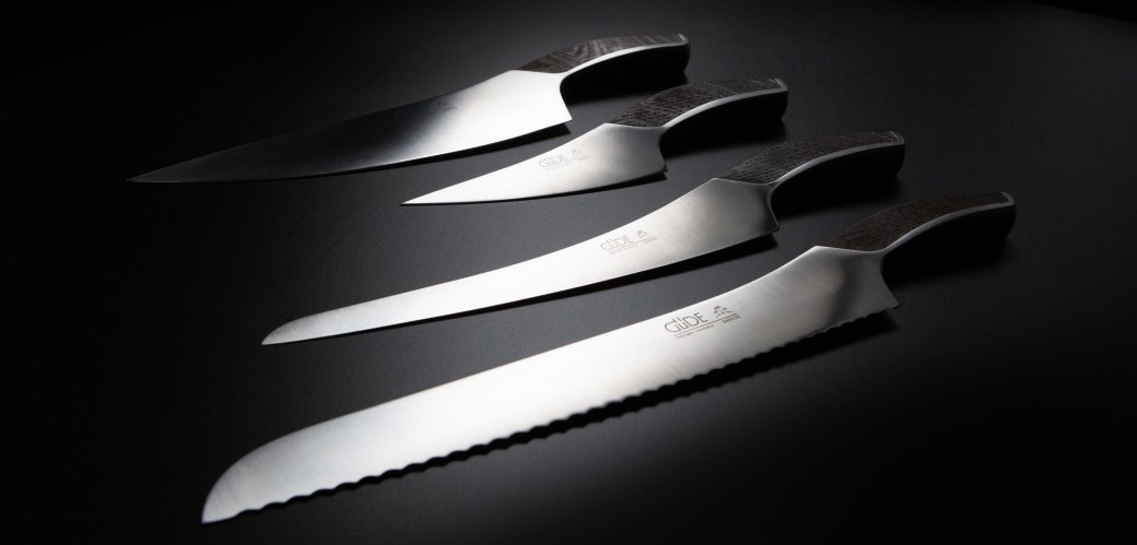 Vier silberfarbene Messer in verschiedenen Größen liegen auf einem schwarzen Untergrund. Der dunkelbraune Holzgriff ist stark geschwungen. Die Klingen sind sehr schlank geschliffen.