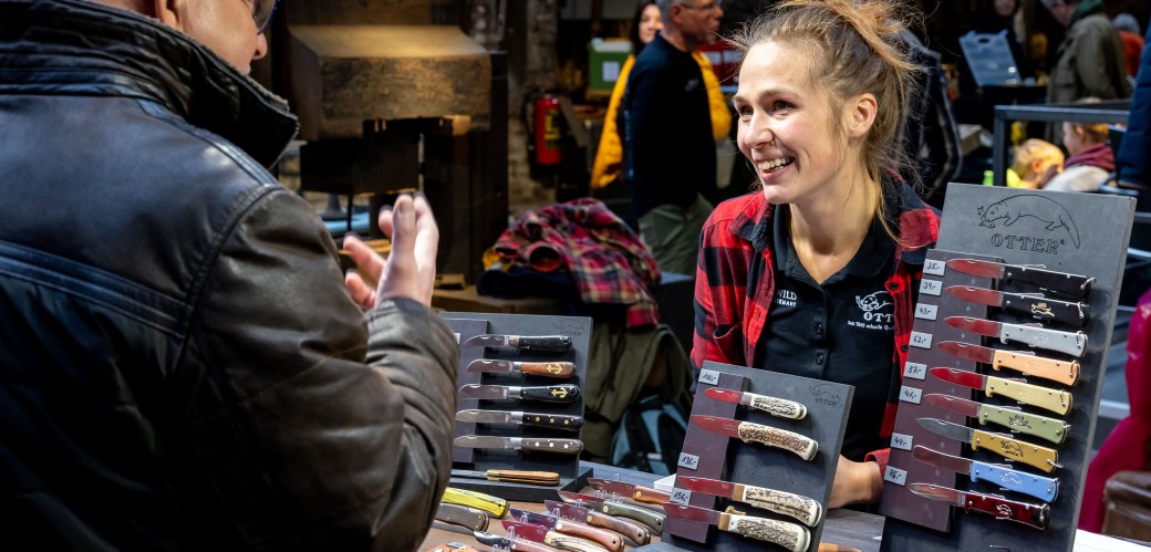 Eine Frau an einem Stand für Taschenmesser berät einen Mann. Sie lächelt freundlich.