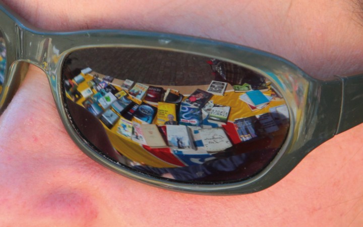 Nahaufnahme einer Sonnenbrille in einem Gesicht, in der sich Bücher spiegeln