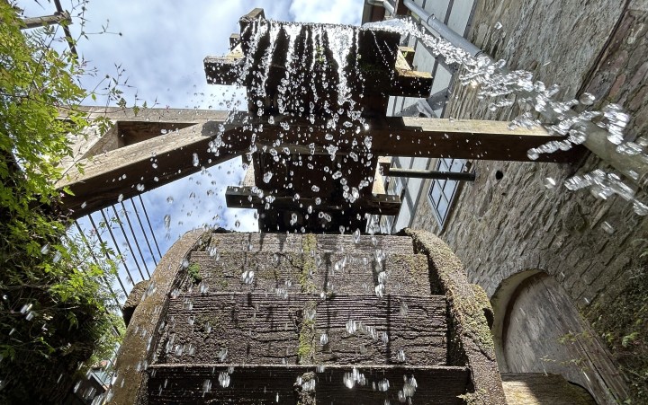Wasserrad einer Papiermühle mit herabfallendem Wasser zwischen steinernen Mauern und Holzträgern.