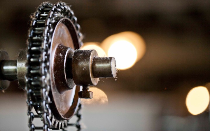 Nahaufnahme eines Metallzahnrads mit Kette vor unscharfem Hintergrund mit Lichtpunkten