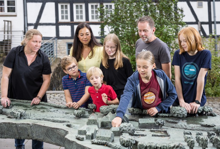 Familie betrachtet ein Modell der Ppiermühle Alte Dombach im Außenbereich.