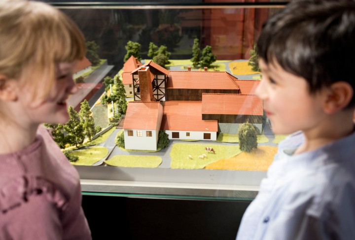 Zwei Kinder schauen sich vor einem Architekturmodell gegenseitig an. 