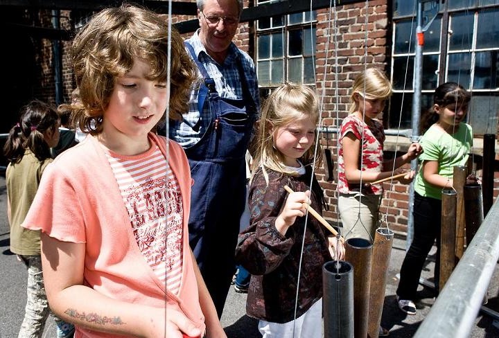 Kinder klopfen mit Stöcken gegen aufgehangene Röhren aus altem Metall. 