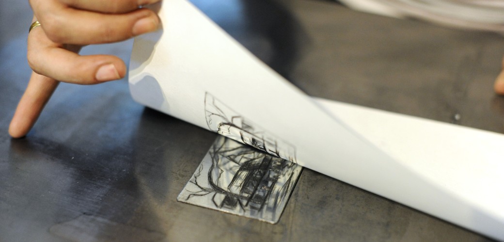 Ein weißes Blatt Papier wird von einer Druckplatte abgezogen. So entsteht ein Abdruck mit schwarzer Tinte auf dem Papier