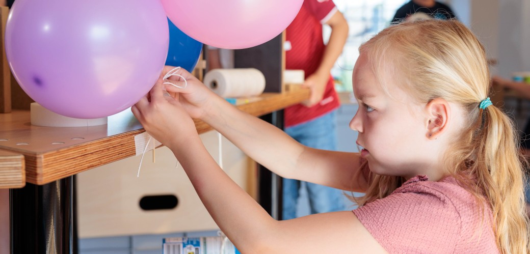 Kind tüftelt an Tisch und klebt Luftballons auf