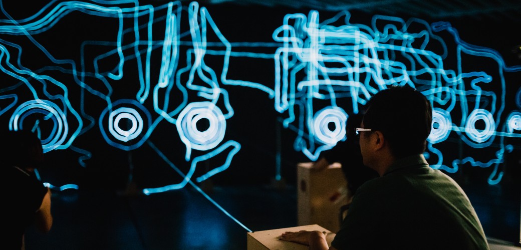 Ein Mann mit Brille und Mütze steht vor einem blau leuchtenden Kunstwerk aus Lichtprojektionen