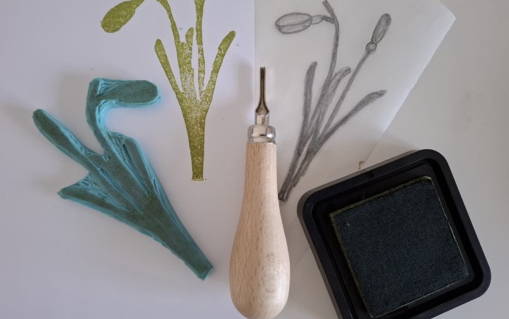 Stempelschnitzwerkzeug mit Holzgriff, daneben ein Stempelkissen, ein grüner Stempel und zwei Papierbögen mit Schneeglöckchenmotiv.