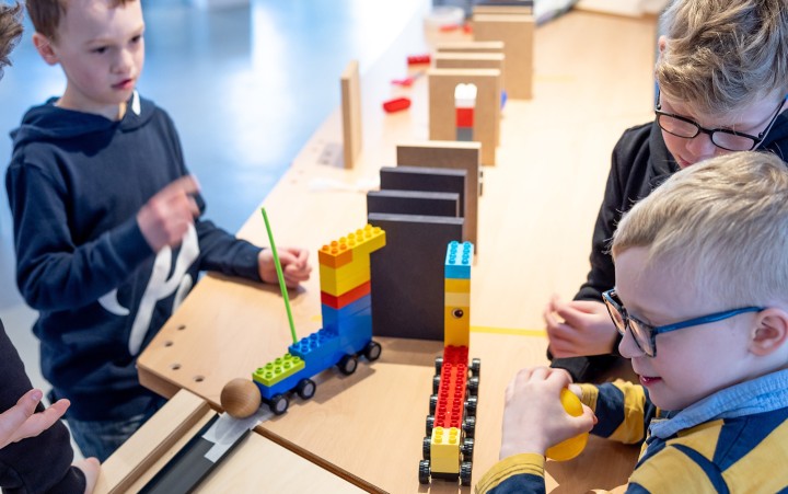 Kinder spielen an einem Holztisch mit bunten Bauklötzen und einer Kugelbahn.