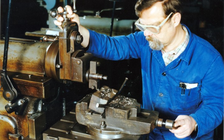 Werkzeugmacher in blauer Arbeitsjacke bedient eine Metallfräsmaschine in einer Werkstatt.