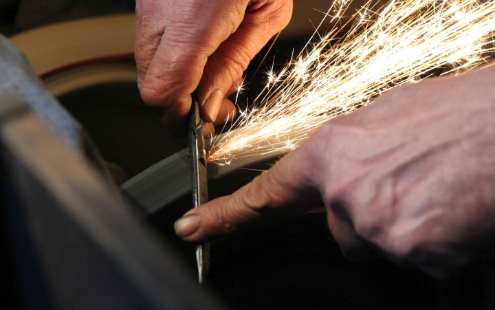 Detailansicht einer Hand, die ein Messer schleift. Dabei sprühen Funken.