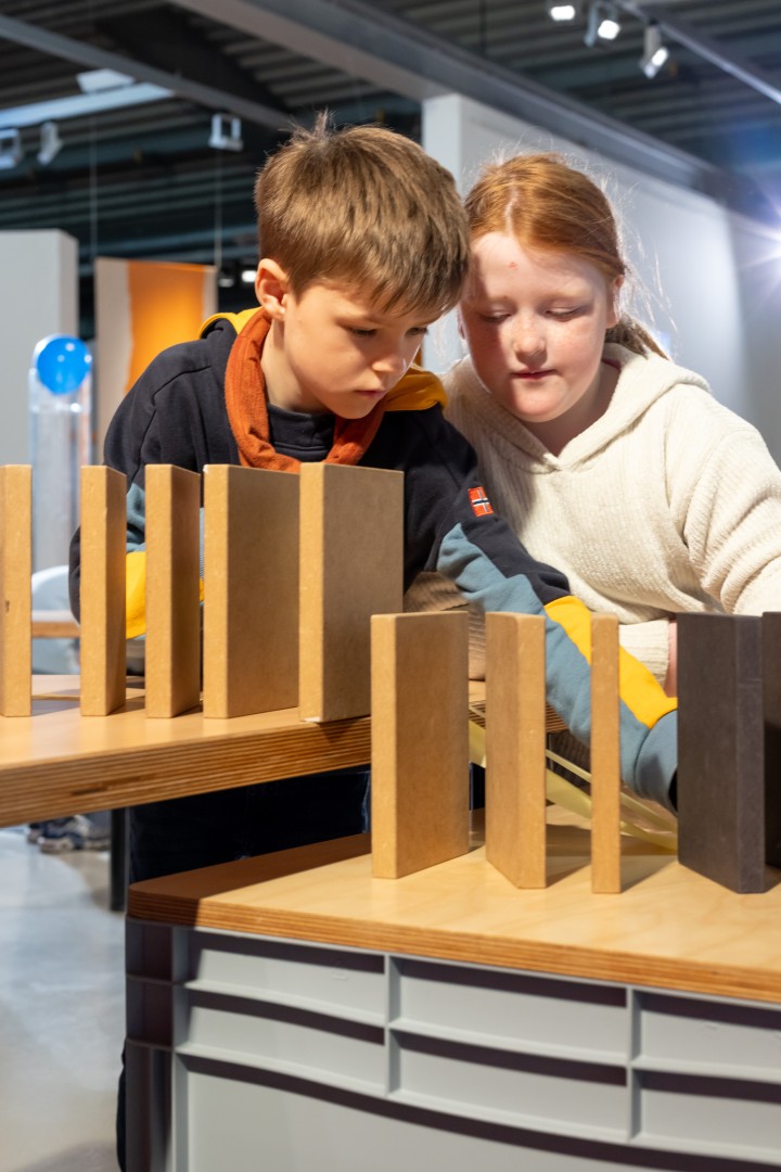 Zwei Kinder stehen an einem Tisch mit aufgestellten Holzklötzen