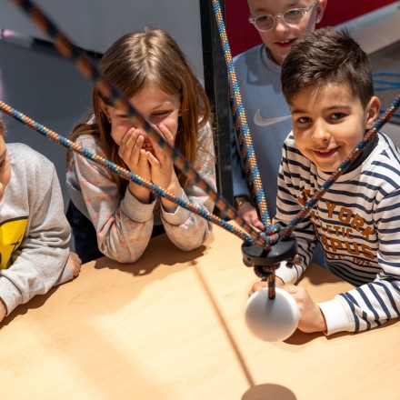 Mehrere Kinder stehen an einem Tisch, über den eine Kugel an einem Seil schwingt